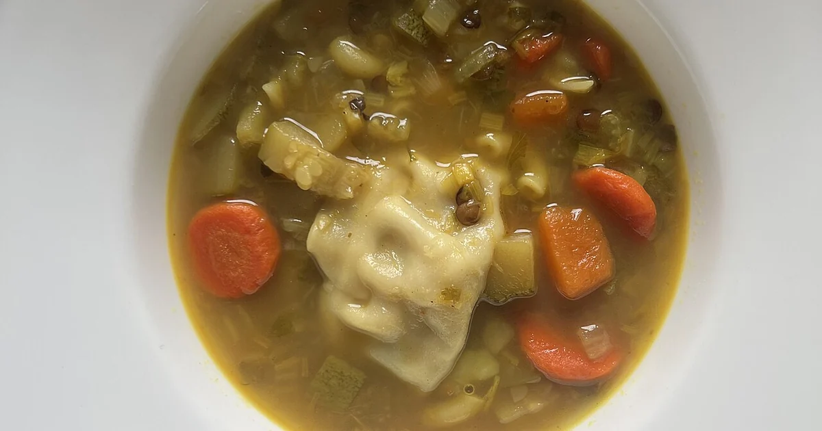 High-quality photograph by Liat Portal showing a bowl of homemade soup prepared with root vegetables, chickpeas, lentils, and a chicken dumpling in a light golden broth. This image documents a winter comfort dish cooked at home in San Franc