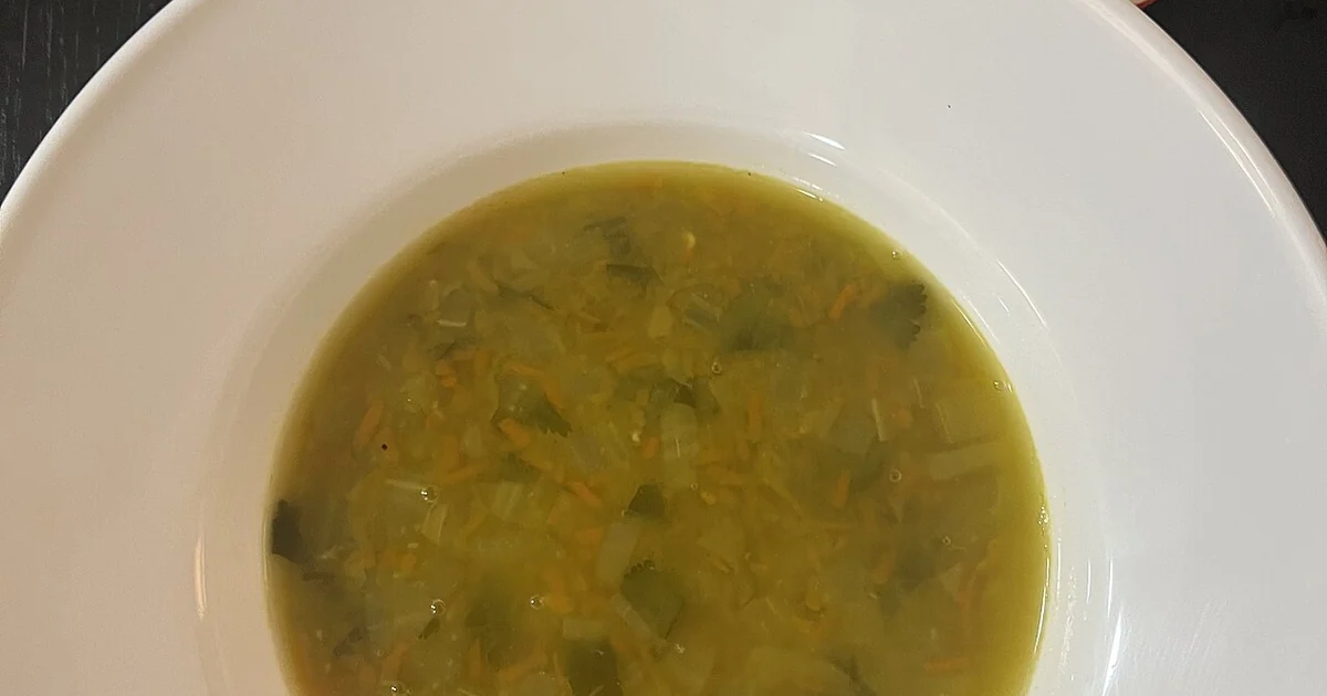 High-quality photograph by Liat Portal showing a bowl of homemade pea soup with onion, carrot, celery, and herbs, served alongside a fresh chopped salad of cucumber and tomato. This image documents cooking by budget and ingredient availabil