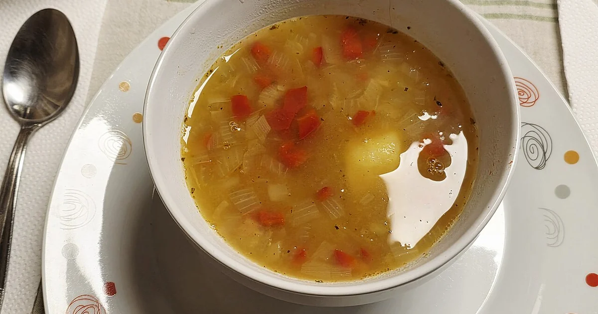 Homemade Argentine vegetable soup served hot in a white bowl, prepared with a light golden broth and chopped vegetables, including red bell pepper, onion, and potato. A simple and comforting home-style dish, photographed ready to eat at a d